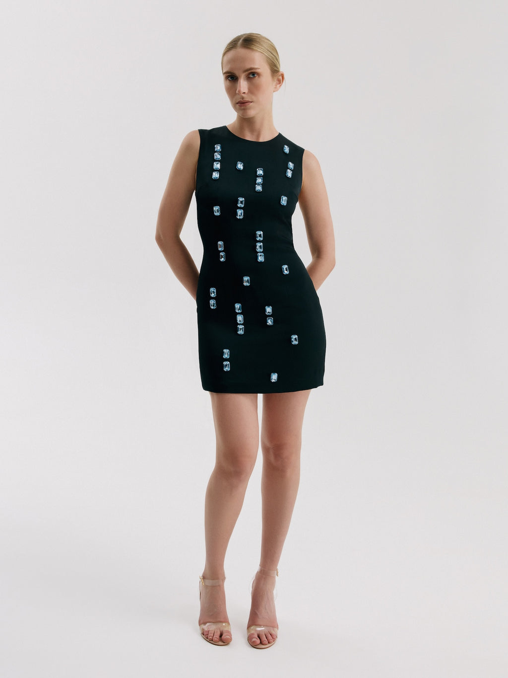 Model wearing black mini dress with large crystal embellishments and structured fit