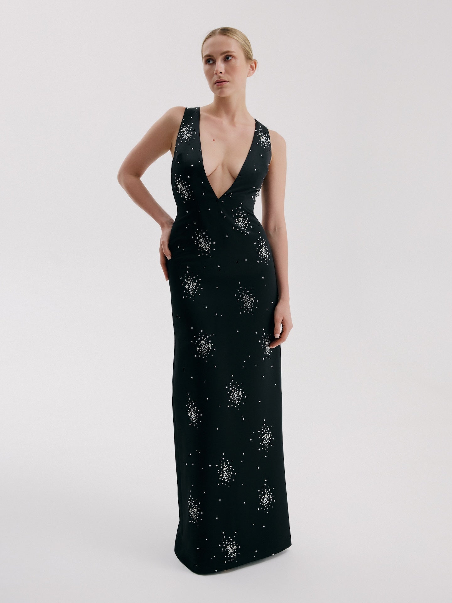 Model wearing black crystal column gown with deep V neckline and fitted silhouette